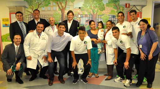 Bone and joint specialists along with medical and nursing staff from the Department of Pediatrics at New York Hospital Queens, and team members from the New York Cosmos, pose for a photo with a young patient with her mother.