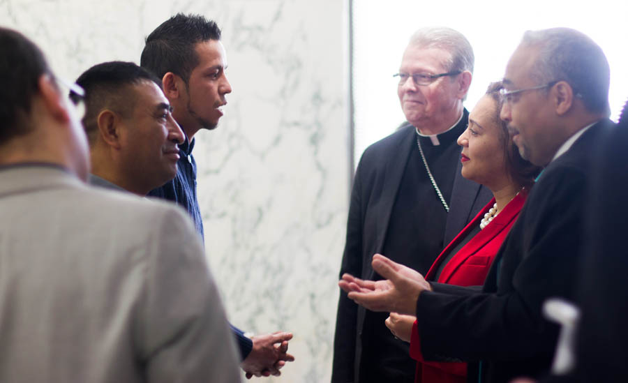 Los senadores estatales Marisol Alcántara y José Peralta, y el obispo católico de Albany, Edward B. Scharfenberger, hablan con  trabajadores agrícolas en Albany.